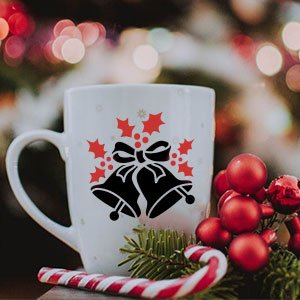 White mug with Christmas bells and holly stencil design, decorated with candy cane and pine sprigs.