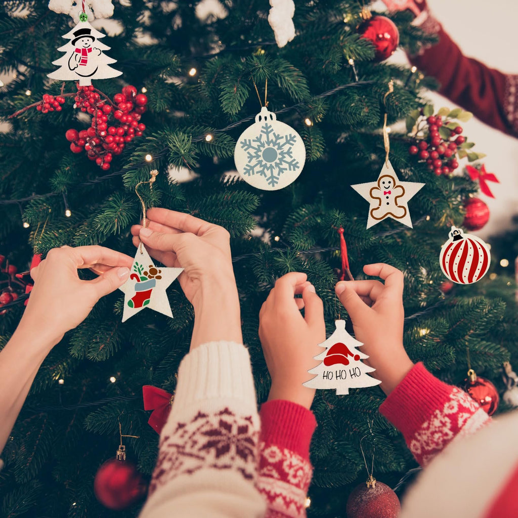 Hands decorating a Christmas tree with stencils of a snowman, snowflake, gingerbread man, stocking, and tree with 'HO HO HO'