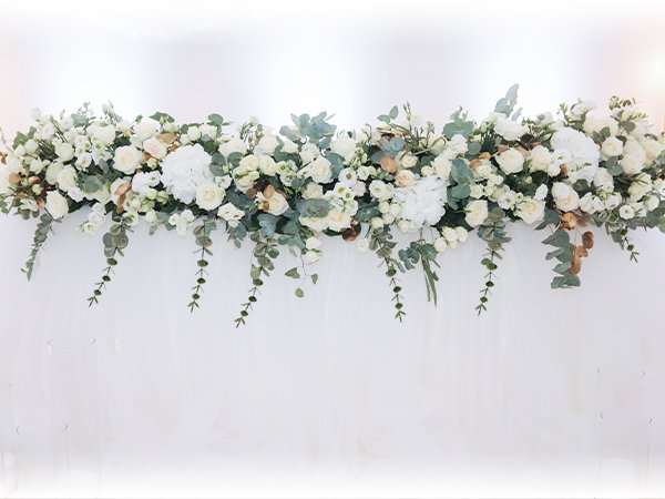 Arrangement of artificial white and cream flowers with eucalyptus leaves, draped across a white background.