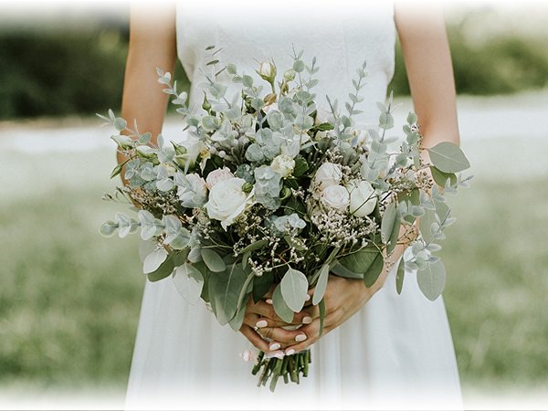 Bride holding a bouquet of artificial eucalyptus stems with white roses and small white flowers