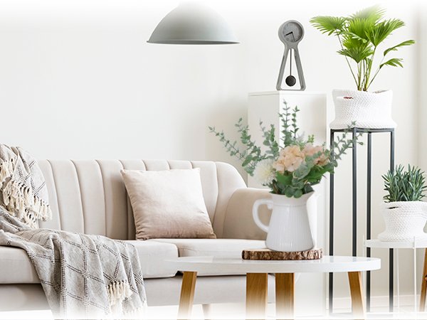 Living room scene with a cream sofa, throw blanket, and coffee table featuring a vase of artificial eucalyptus and flowers.