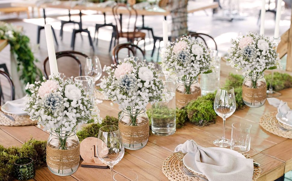 Table setting with floral arrangements of white baby's breath and pink, blue, and white flowers in jars.