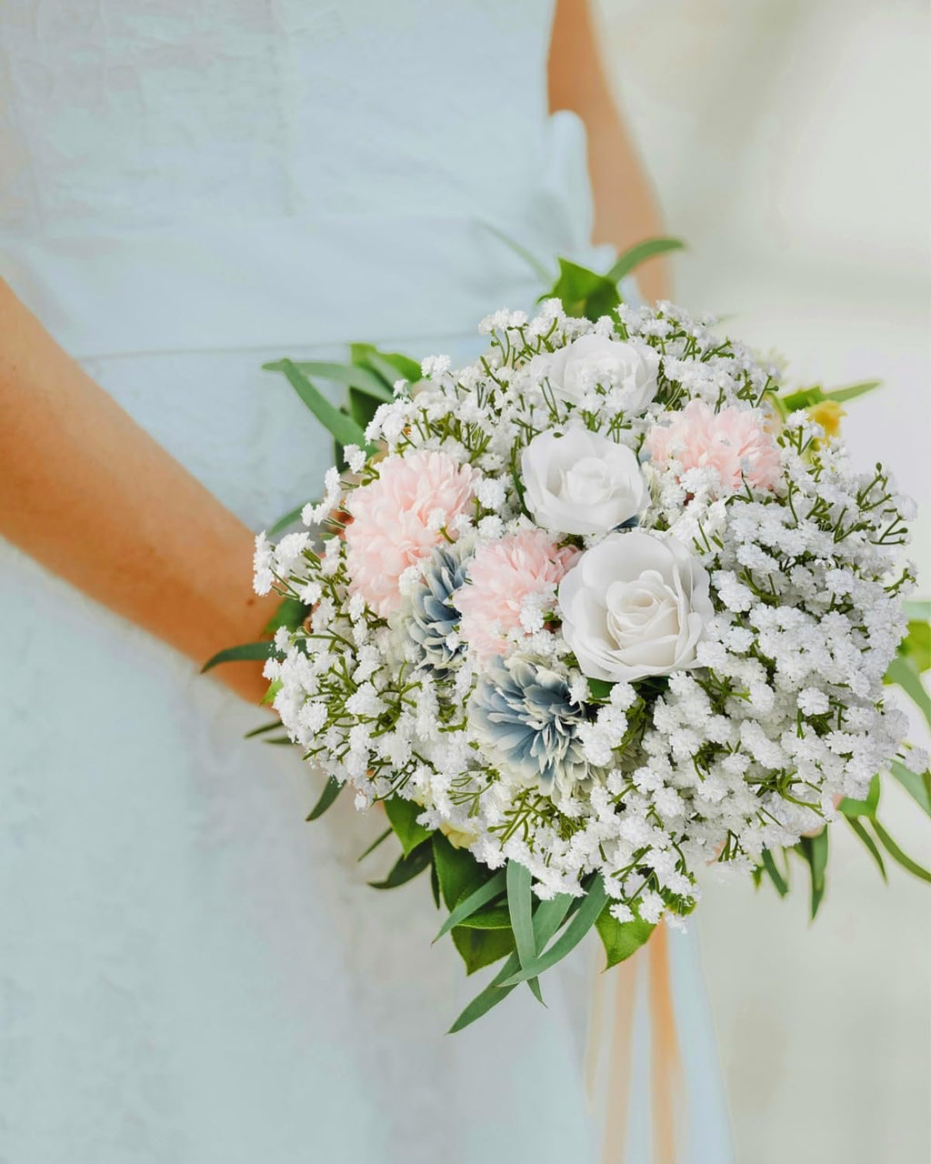 Bride holding a bouquet of white, pink, and blue artificial flowers with baby's breath and greenery.