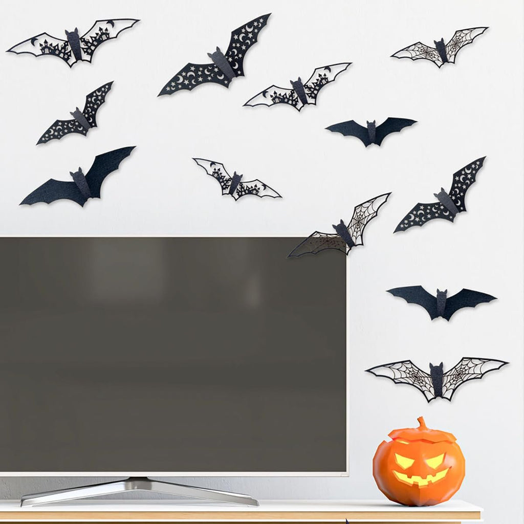Black 3D vinyl Halloween bat wall stickers in various sizes and designs, some with moon and star patterns, arranged on a white wall above a television and a jack-o'-lantern.
