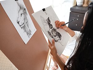 Artist sketching a butterfly and skull on paper with charcoal pencils, lion drawing on easel nearby
