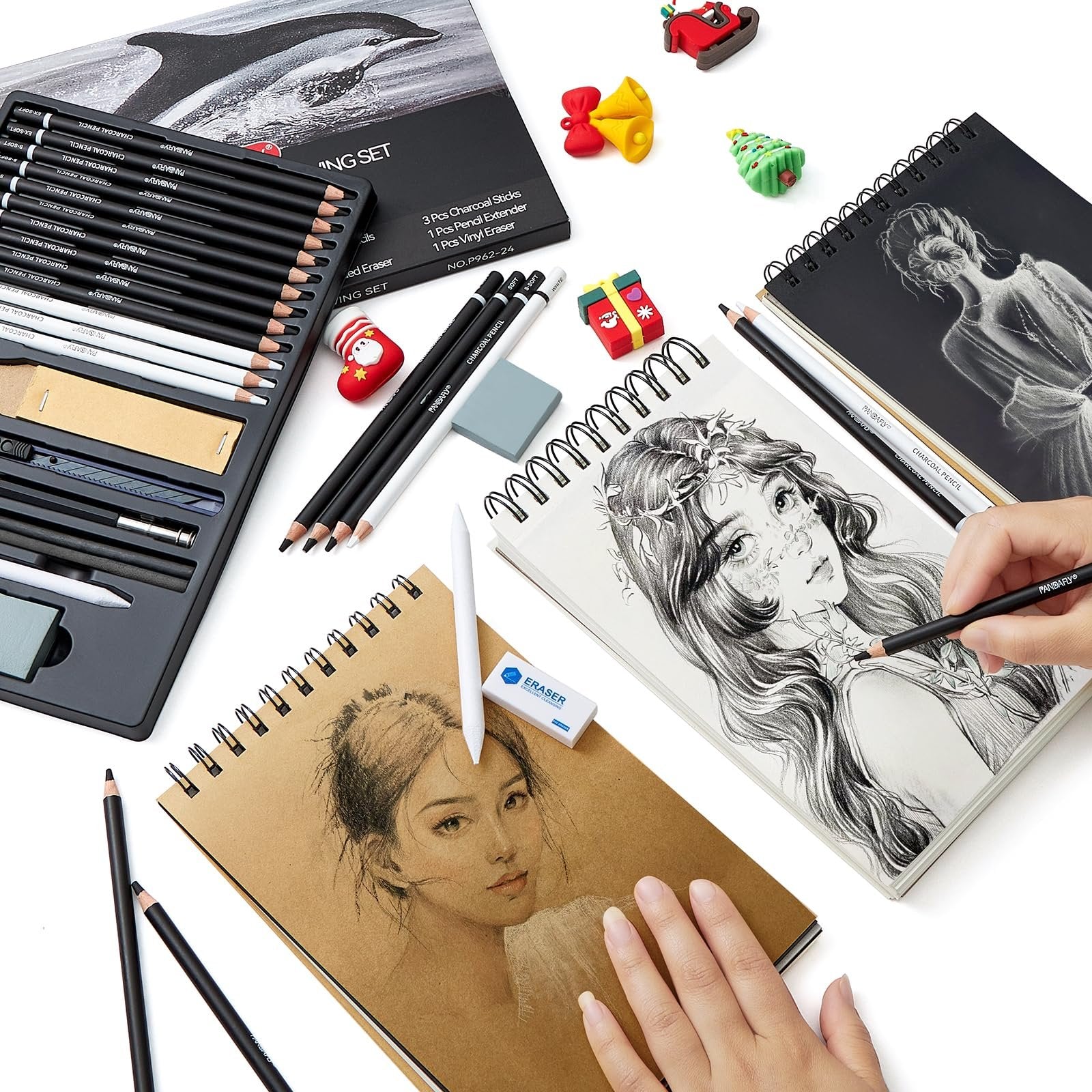 Charcoal drawing set with pencils, sketchbooks, and erasers, arranged on a white surface.