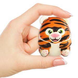 Hand holding a small, slow-rising squishy toy shaped like a cartoon tiger with orange and black stripes.