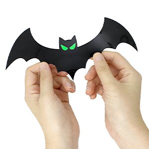 Hands holding a black magnetic bat Halloween decoration with glowing green eyes against a white background.