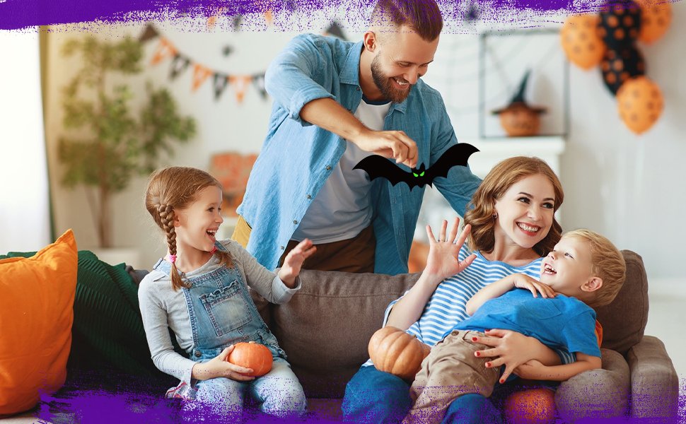 Family celebrating Halloween indoors, with a father holding a bat decoration for his children.