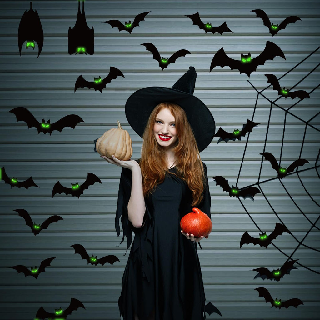 Woman in witch costume holding pumpkins surrounded by glow-in-the-dark bat decorations and a spider web