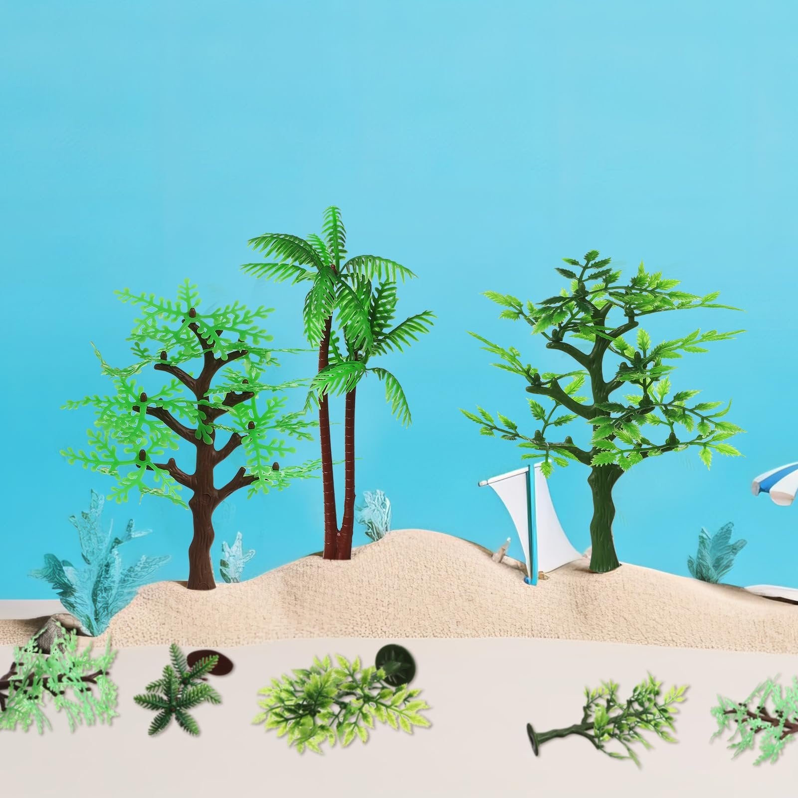 Plastic jungle trees and foliage arranged on sand with a blue background, featuring a sailboat and umbrella.