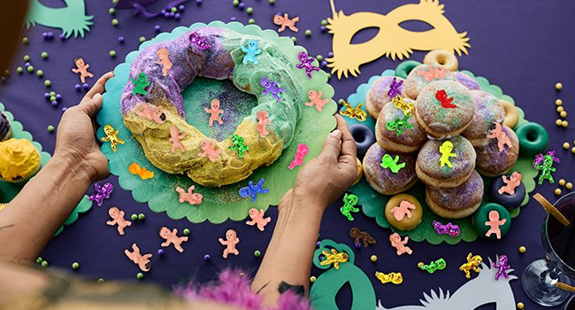 Mardi Gras king cake and donuts decorated with small plastic baby figures and sprinkles, overhead view.