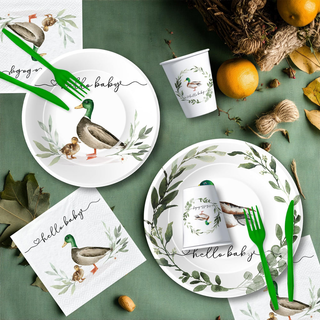 Mallard duck themed baby shower party supplies including plates, cups, and napkins with green cutlery on a green tablecloth.
