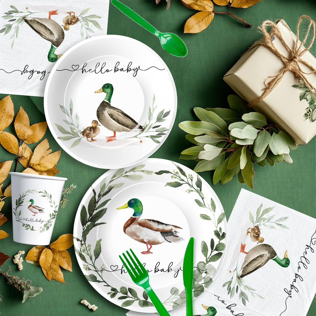 Mallard duck themed baby shower party supplies including plates, cups, napkins, and cutlery arranged on a green tablecloth with autumn leaves and a gift.