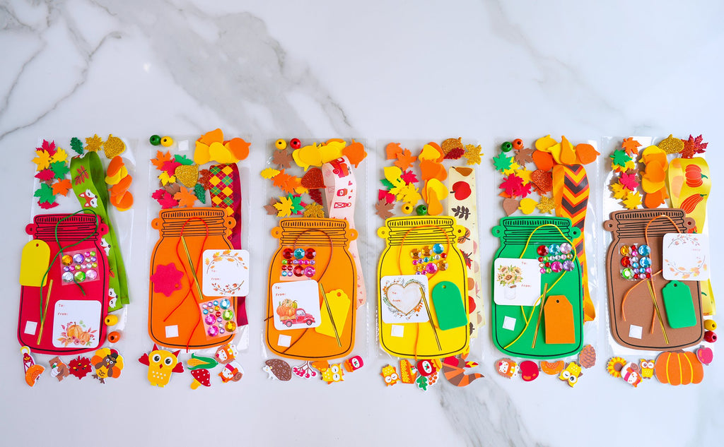 Fall mason jar craft kits with foam bases, stickers, beads, tags, and cords laid out on a white marble surface.