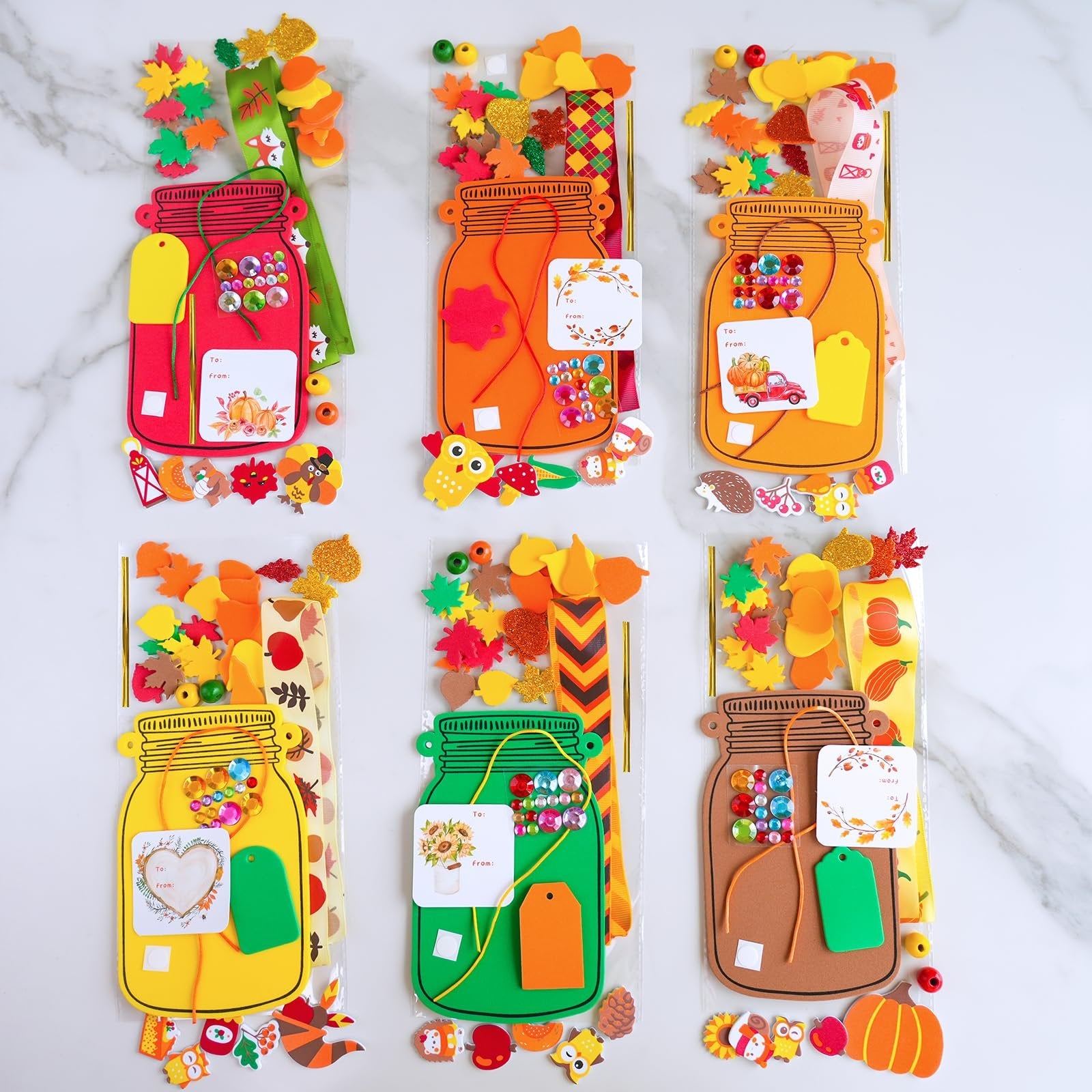 Six fall mason jar ornament craft kits displayed on a marble background, each kit contains foam bases, stickers, beads, tags, cords, and instructions.
