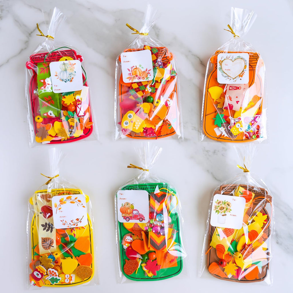 Six fall mason jar craft kits filled with foam shapes, stickers, beads, and tags on a marble surface.
