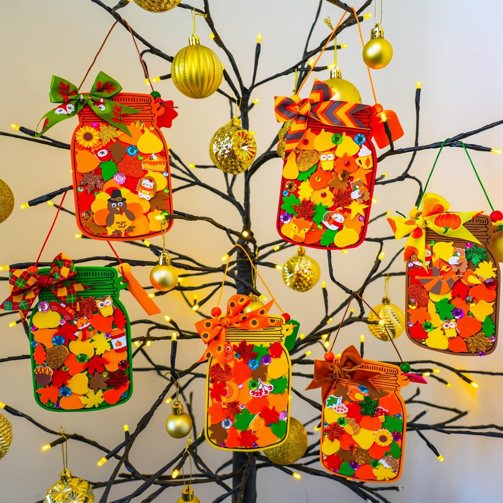 Fall mason jar ornaments decorated with autumn leaves, pumpkins, and animals hanging on a decorative tree with lights.