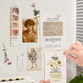 Silver magnetic push pins holding various art prints and photos on a wall, with a hand placing one pin.