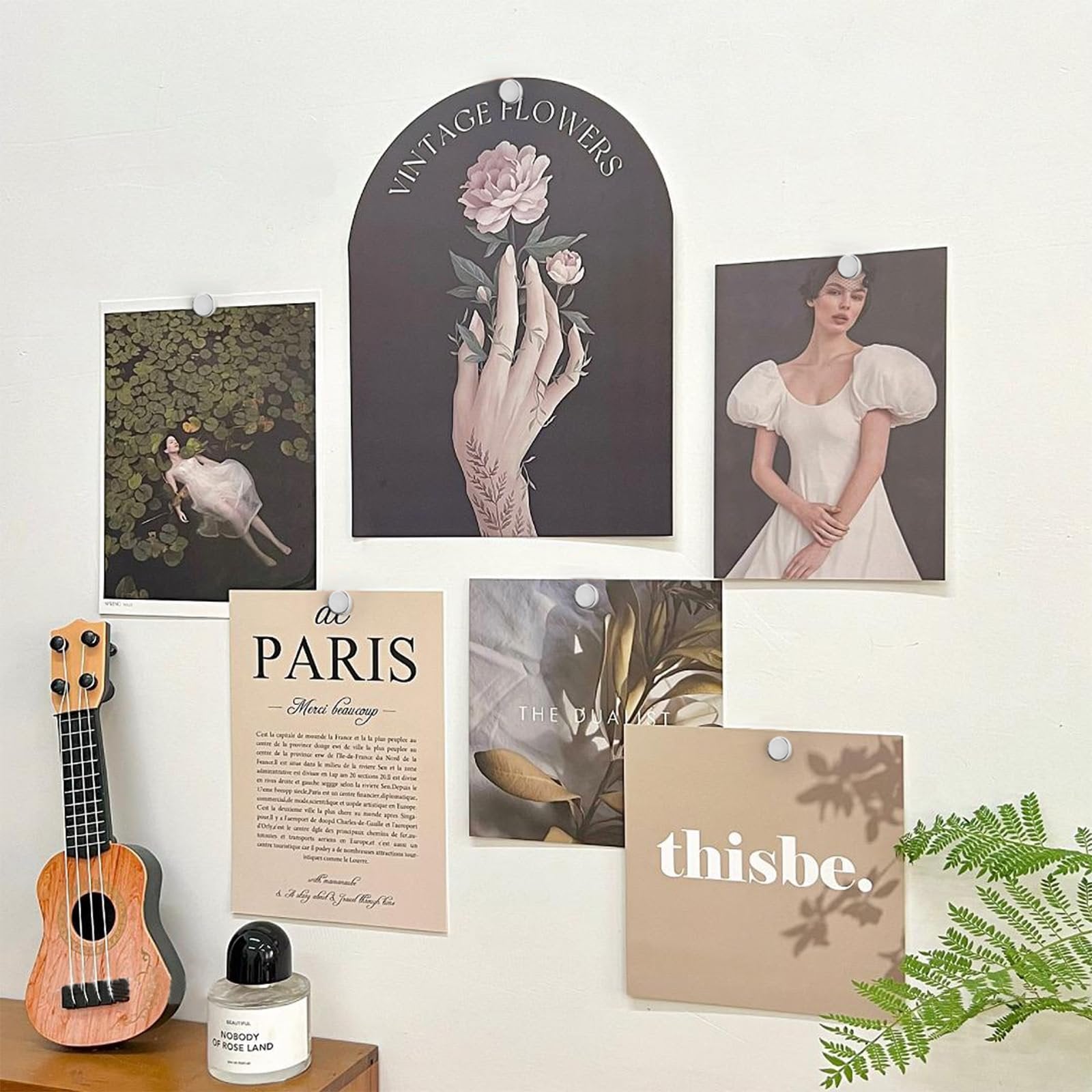 Collage of decorative prints and a ukulele on a white wall, held by push pins.
