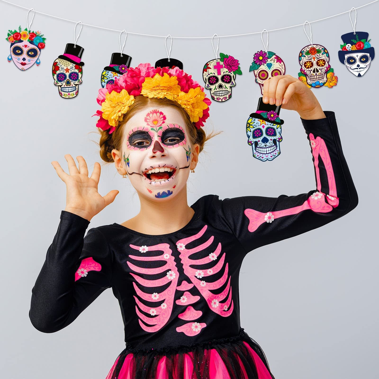 Girl in skeleton costume with sugar skull face paint holds a sugar skull ornament hanging from a string