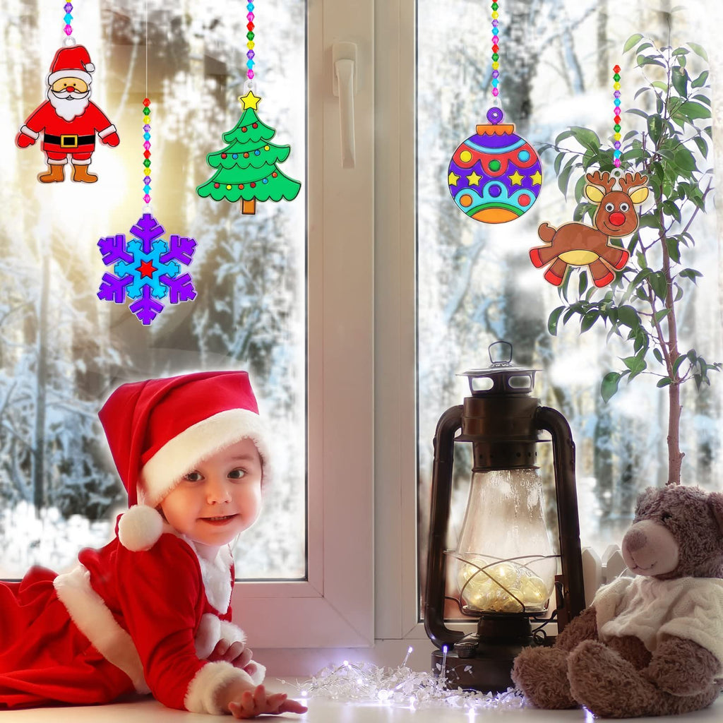 Christmas suncatcher crafts hanging in window with baby in Santa costume, lantern, and teddy bear