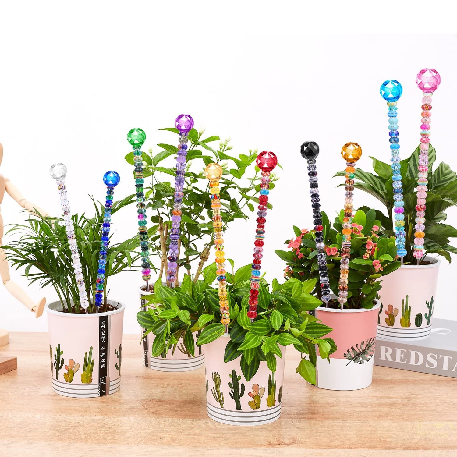 Assortment of colorful beaded plant stakes in pots with decorative cactus designs.