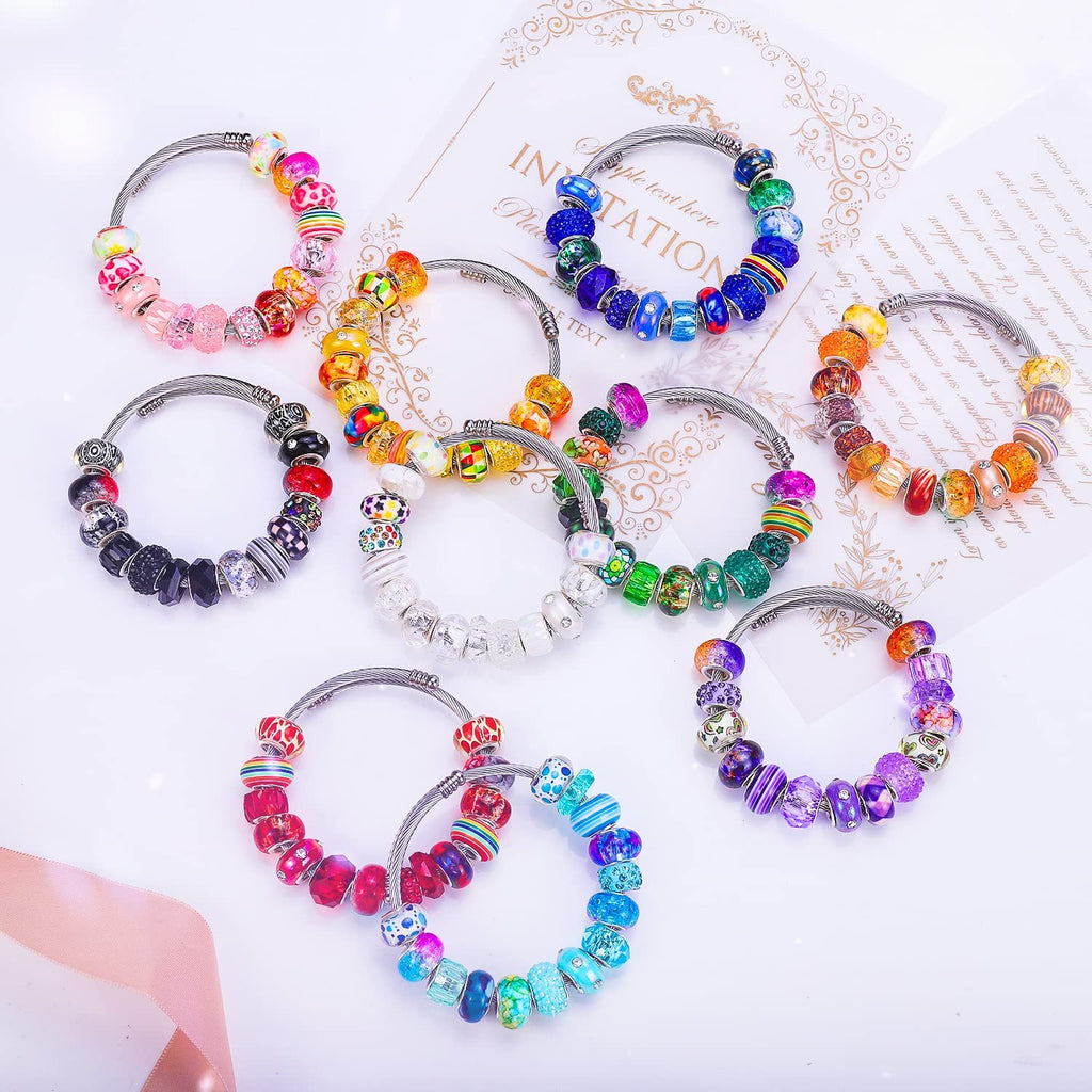 Assortment of DIY charm bracelets with colorful lampwork spacer beads on white background with decorative paper