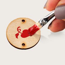 Hand painting a red heart design onto a blank wooden circle tag with two holes