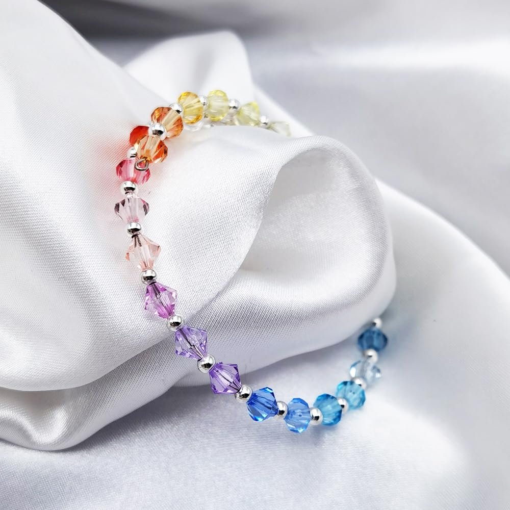 Rainbow gradient faceted bicone acrylic beads bracelet with silver spacer beads on white satin fabric.