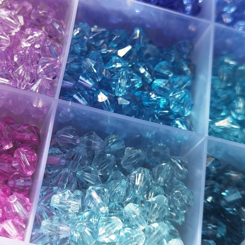Close-up of faceted acrylic bicone beads in a divided plastic organizer, showing pink, blue, and clear beads.