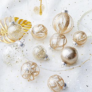 Collection of clear and champagne glitter-filled Christmas ball ornaments with gold designs, arranged on a white sparkly surface.