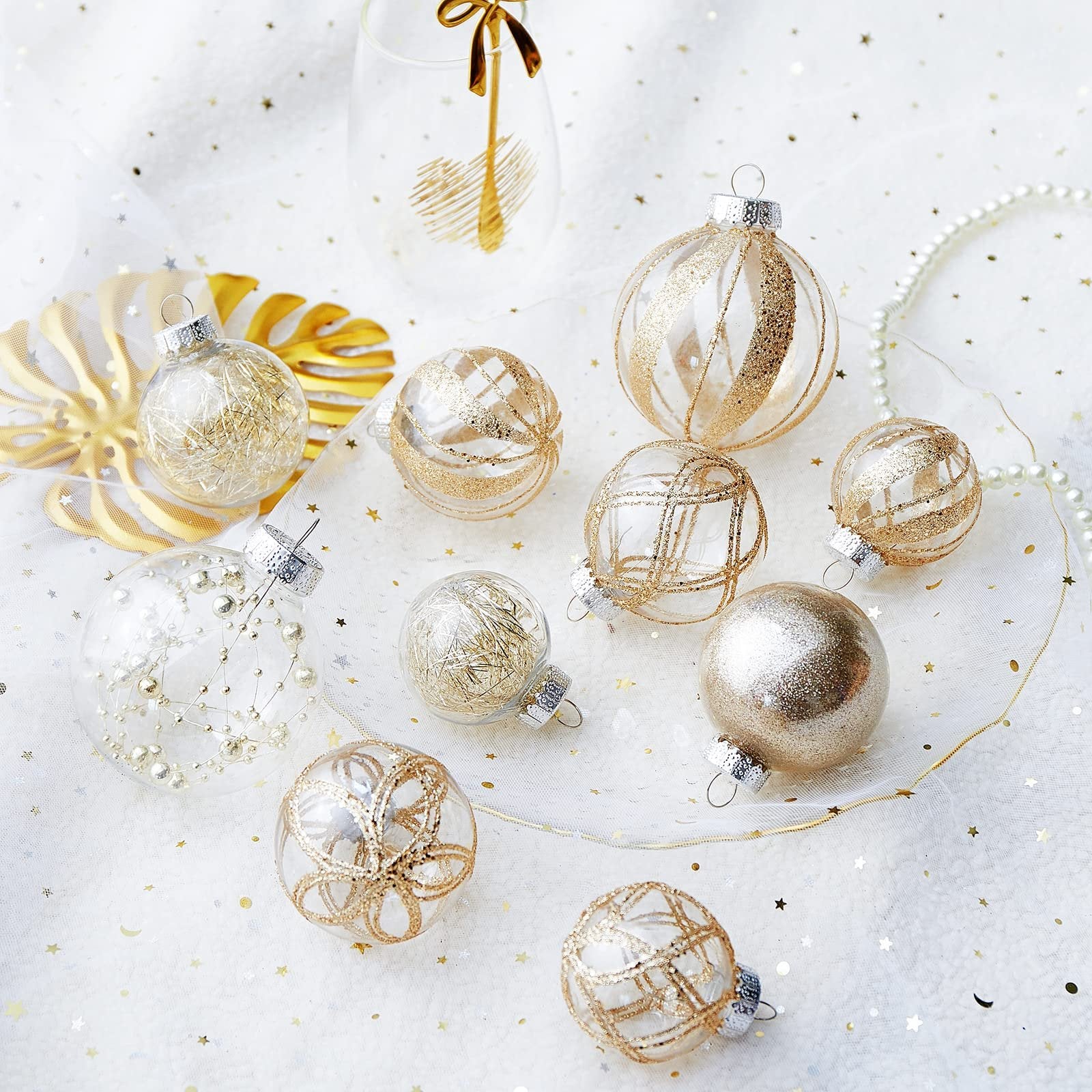 Assortment of clear plastic Christmas ball ornaments with gold glitter fill and designs, arranged on a white sparkly surface.