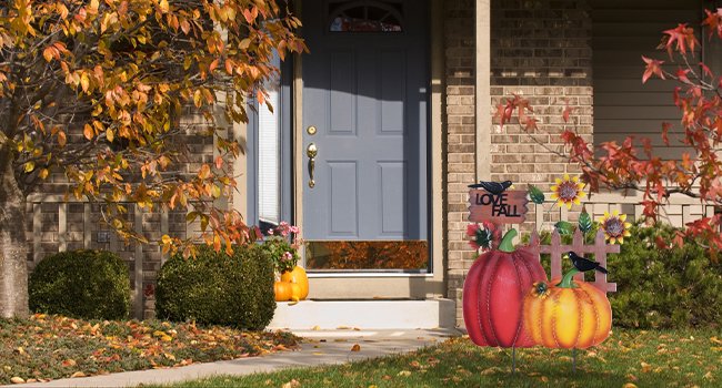 Decorative metal fall garden stake with pumpkins, sunflowers, crows, and 'I LOVE FALL' sign placed in front of a house entrance.