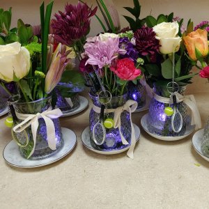 Assortment of small floral arrangements in clear glass vases with tennis racket and ball charms, tied with ribbon.
