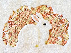 White rabbit embroidered on a textured background with autumn leaves pattern