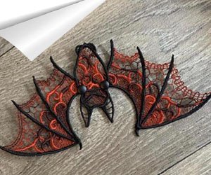 Black and orange lace bat applique with button eyes, lying flat on a wooden surface.