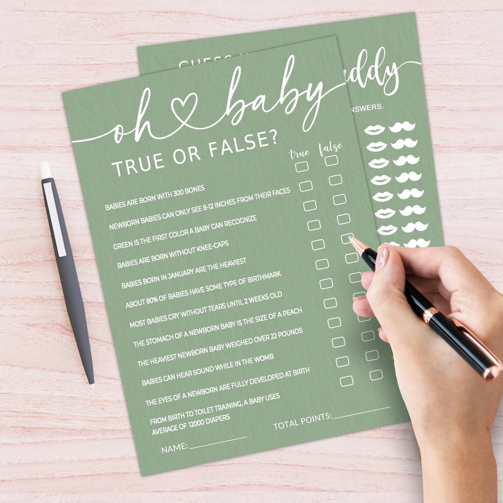 Baby shower game cards with 'Oh Baby' and 'True or False' prompts, a hand holding a pen to fill them out.