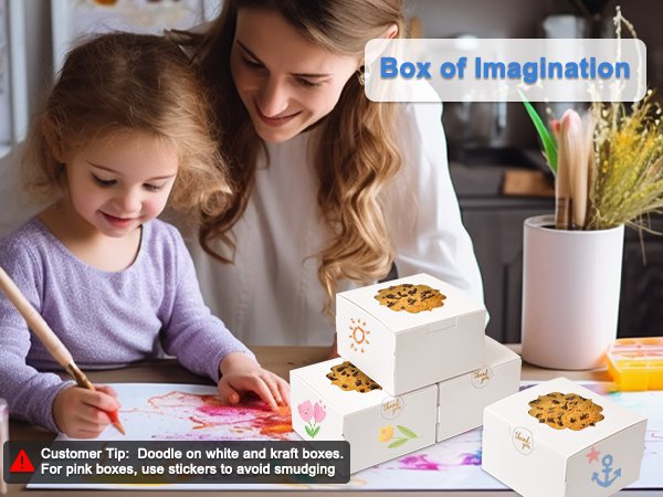 Mother and daughter decorating white treat boxes with cookies on top, one box has an anchor design.