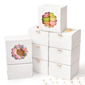 Stack of white bakery boxes with clear windows, one showing a pink frosted donut and another showing macarons.