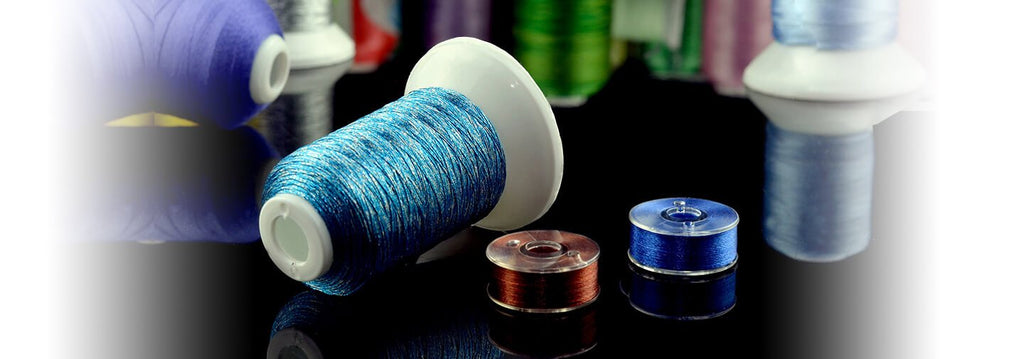 Close-up of blue and brown prewound bobbins with thread, on a reflective black surface, with blurred spools in the background.