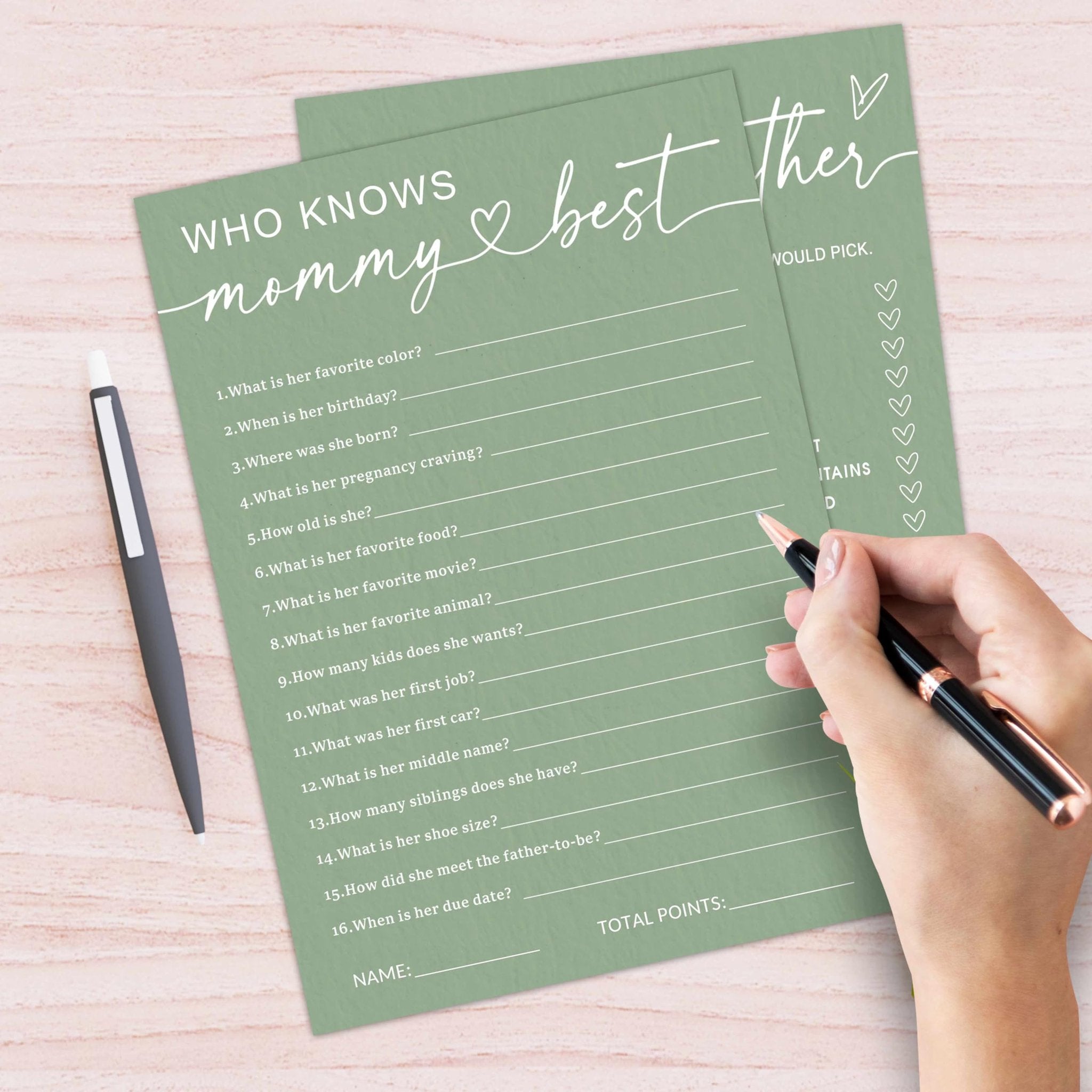 Baby shower game cards with questions about the mother-to-be, held by a hand with a pen.