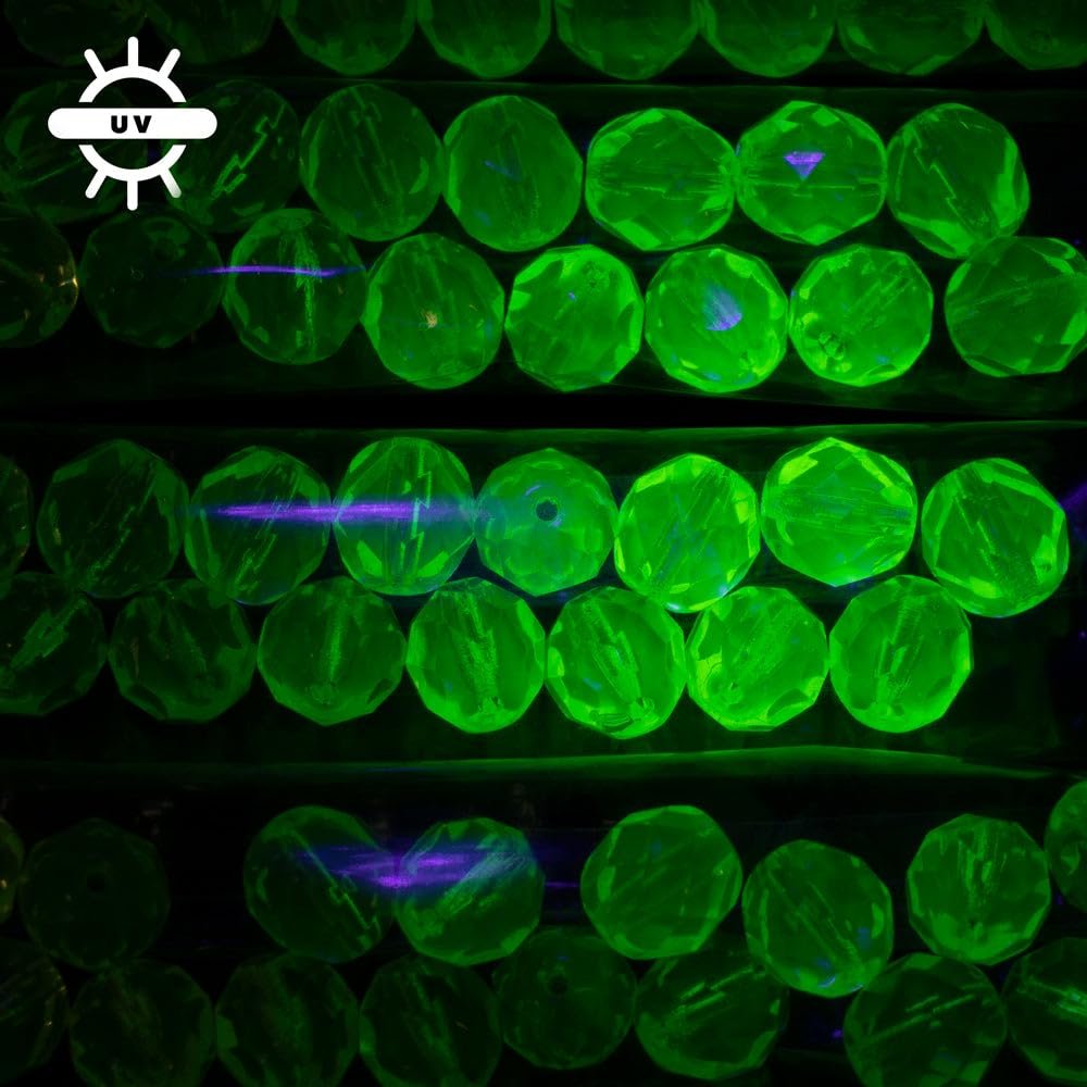 Rows of faceted glass beads glowing bright green under UV light, showing internal facets and some purple light reflections.