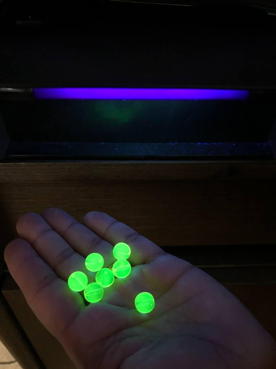 Hand holding several glowing green faceted glass beads under a blacklight