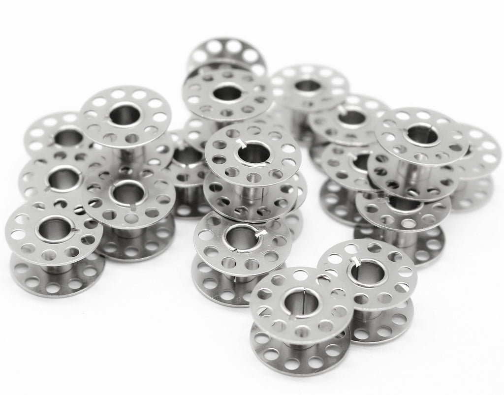 Pile of metal sewing machine bobbins on a white background, close-up shot showing multiple bobbins stacked and scattered.