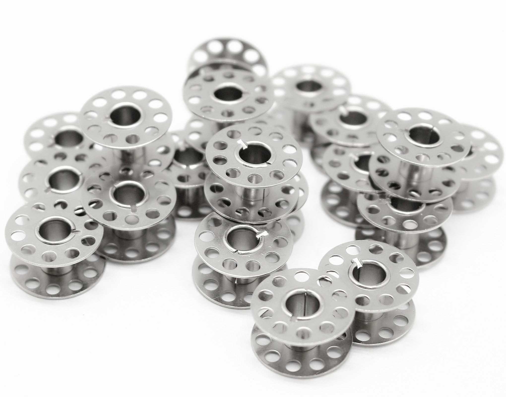 Pile of metal sewing machine bobbins on a white background, close-up shot showing multiple bobbins stacked and scattered.