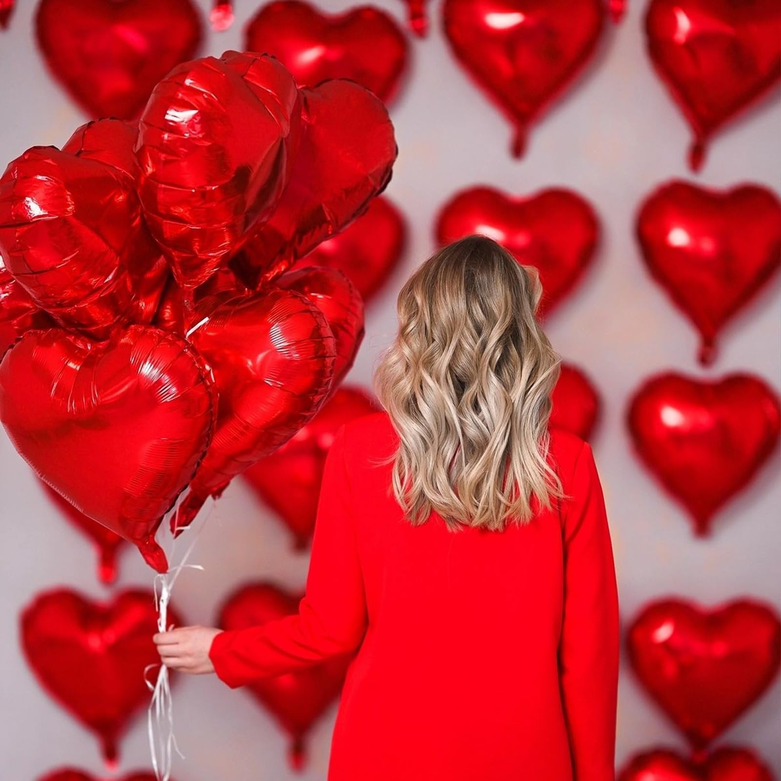 Woman in red holding a bouquet of red heart-shaped foil balloons against a backdrop of red heart balloons