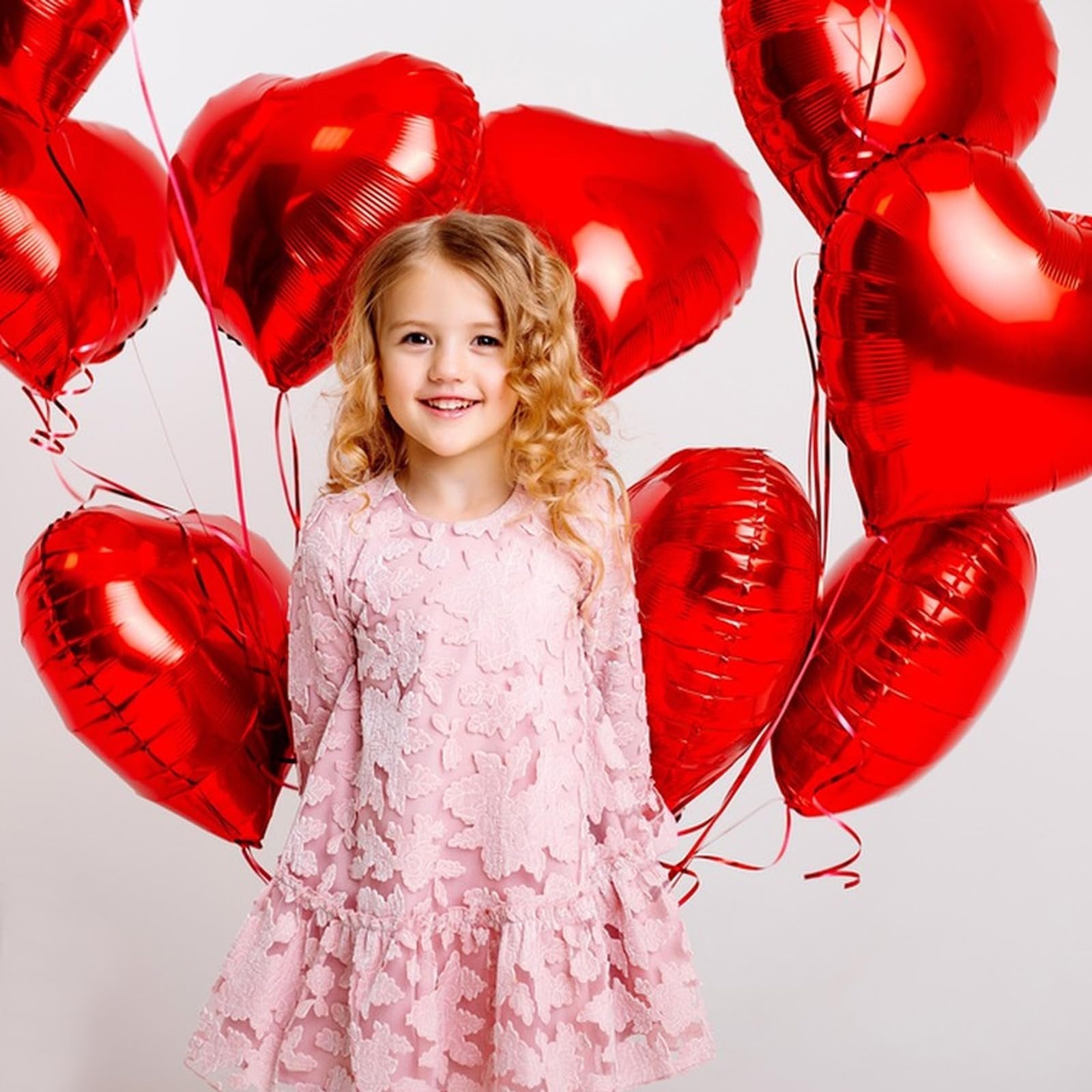 Smiling young girl in a pink dress surrounded by red heart-shaped balloons
