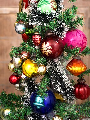 Assortment of vintage glass Christmas ornaments in various shapes and colors hanging on a decorated tree.