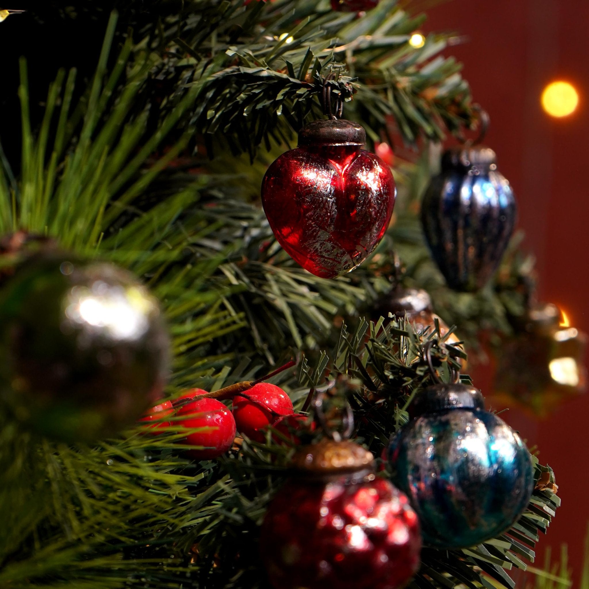 Close-up of vintage glass Christmas ornaments in red and blue hanging on a pine tree branch with red berries.